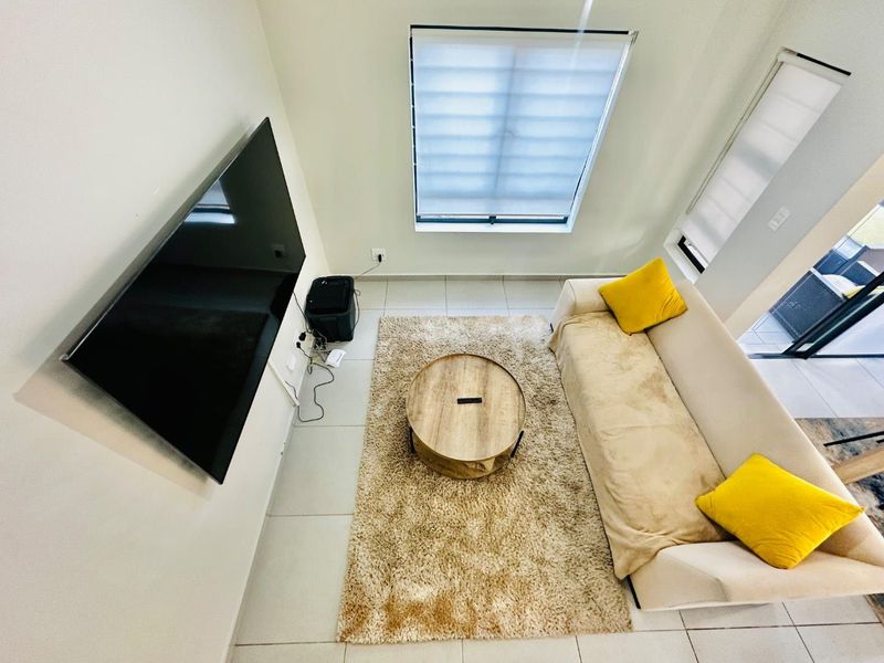 A bright, modern living room featuring tiled flooring, large windows with roller blinds, and direct access to an outdoor patio area.