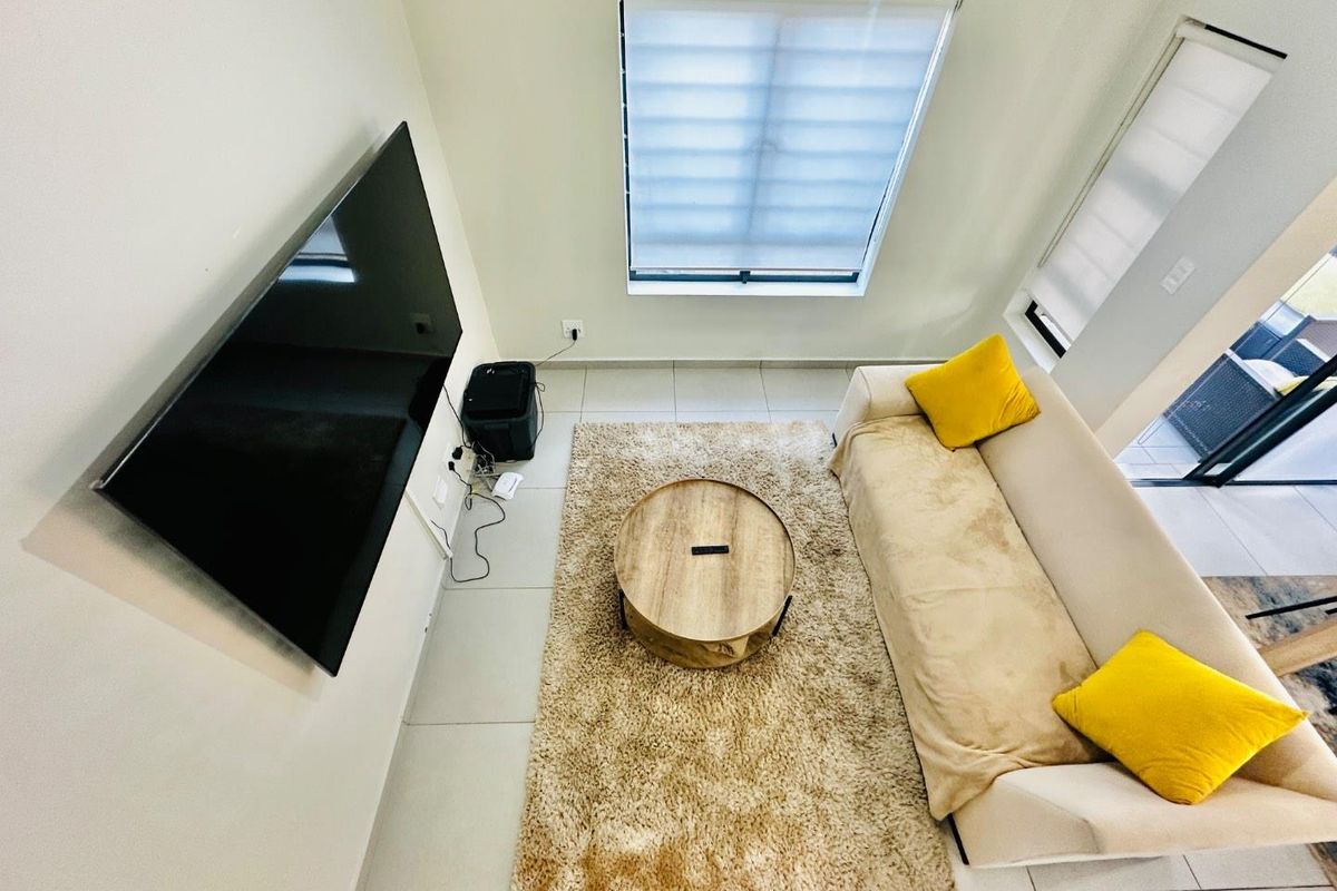 A bright, modern living room featuring tiled flooring, large windows with roller blinds, and direct access to an outdoor patio area.