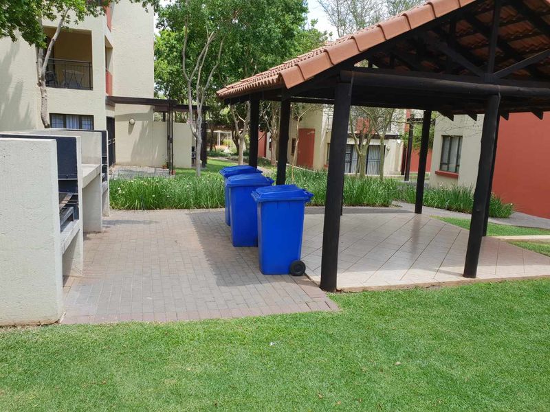 Communal outdoor area featuring a built-in braai, a covered gazebo with tiled flooring, and surrounding landscaped garden space within the apartment complex.