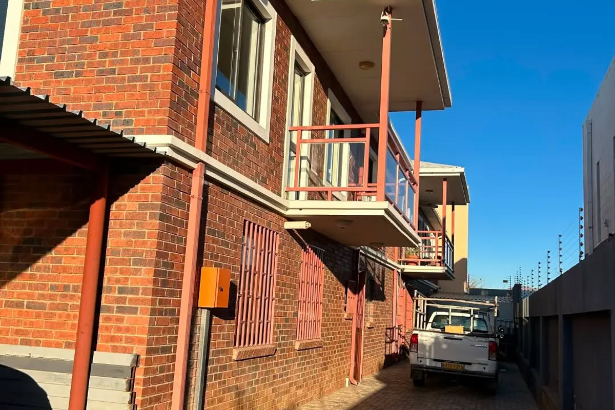 Exterior view of the apartment building featuring face brick construction, balconies with metal railings, and a paved driveway with perimeter electric fencing.