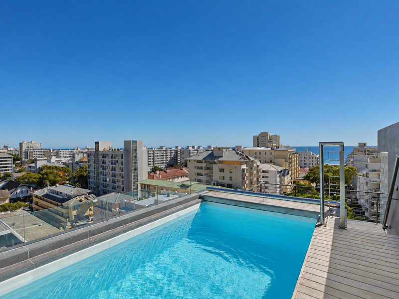 A rooftop swimming pool featuring timber decking, glass balustrades, and panoramic urban and ocean views.