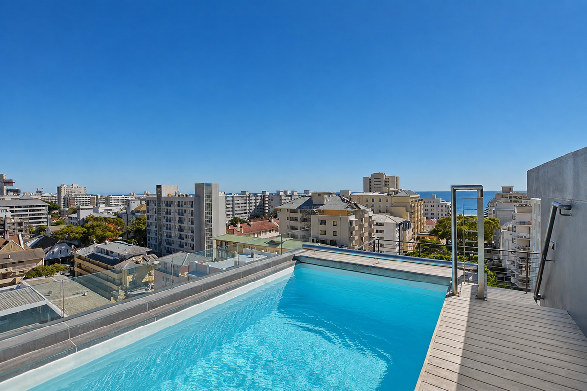 A rooftop swimming pool featuring timber decking, glass balustrades, and panoramic urban and ocean views.