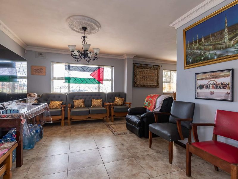 A spacious living room featuring tiled flooring, decorative ceiling rose with a chandelier, and classic cornice detailing, providing a comfortable and functional family space.
