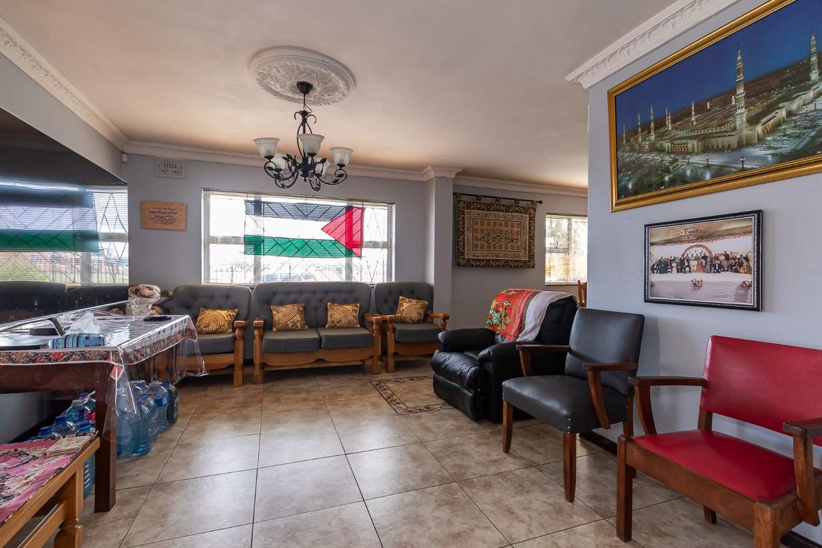 A spacious living room featuring tiled flooring, decorative ceiling rose with a chandelier, and classic cornice detailing, providing a comfortable and functional family space.