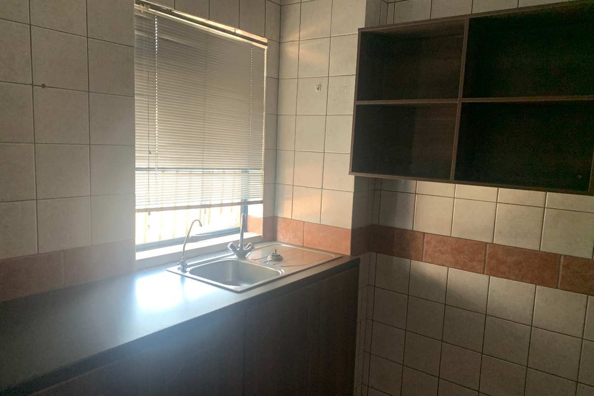 A functional office kitchenette featuring a stainless steel sink, tiled splashbacks, and built-in cabinetry for storage.