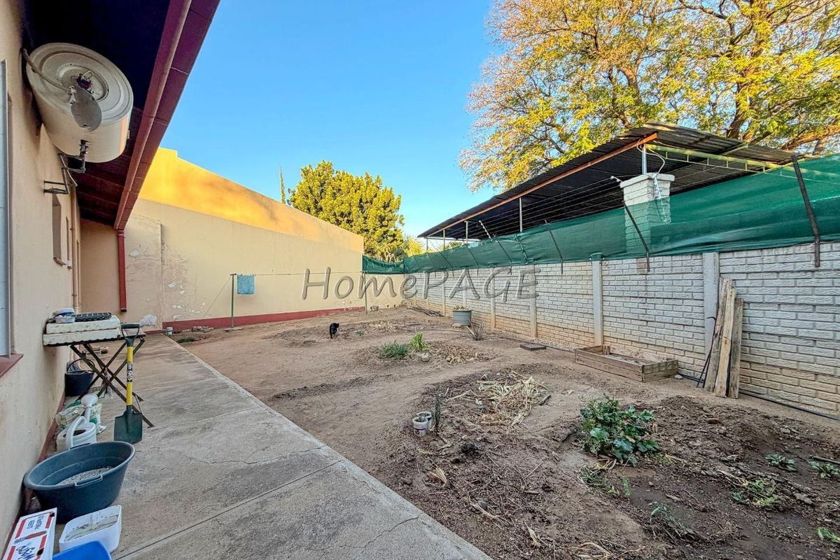 Rear exterior view featuring a concrete patio, brick boundary wall with shade screening, and an unlandscaped garden area requiring maintenance.