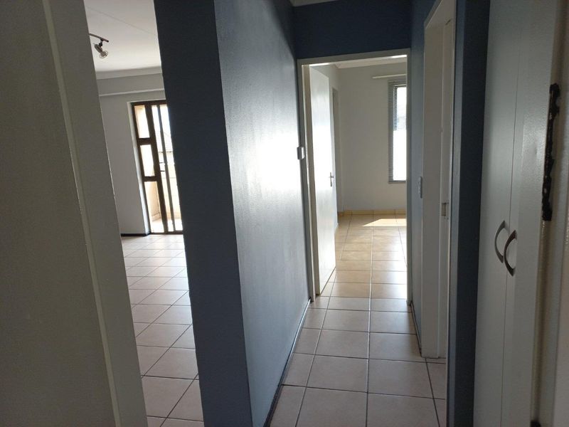 A bright, empty hallway featuring tiled flooring and built-in storage, providing access to adjacent living areas and rooms within the apartment.