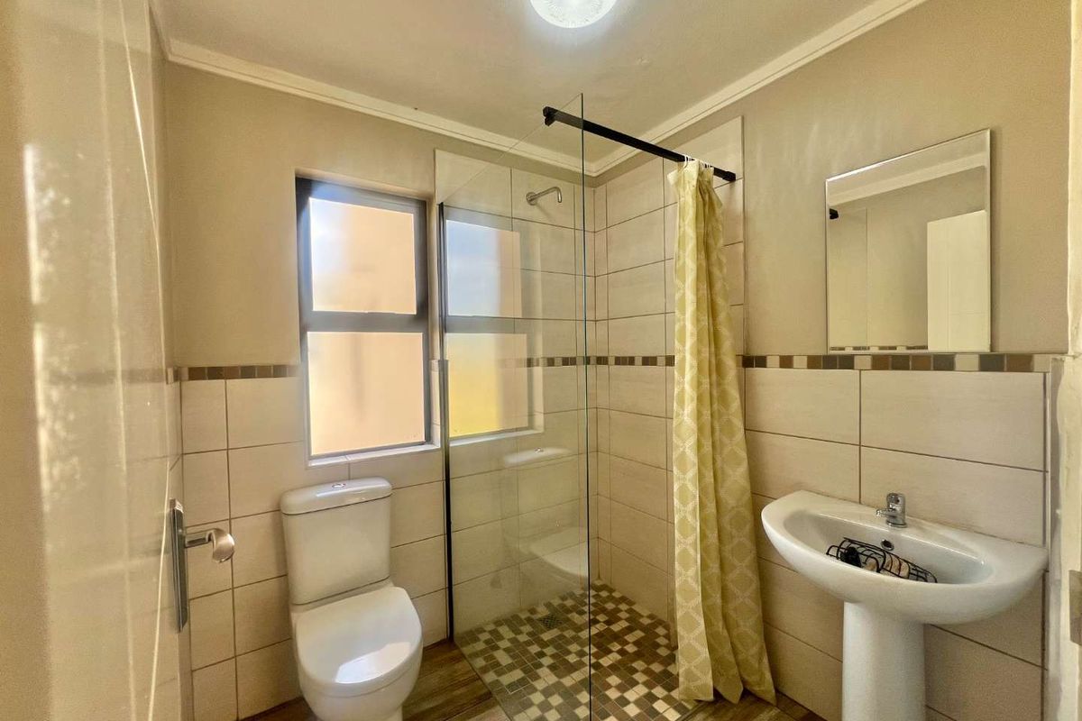 A functional bathroom featuring a glass-enclosed walk-in shower, pedestal basin, and toilet with neutral wall tiling and wood-look floor tiles.