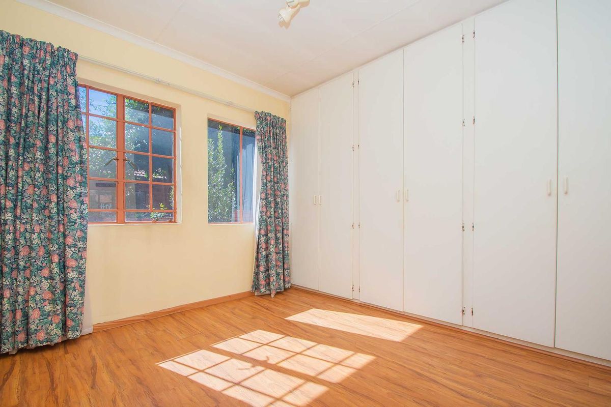 A bright bedroom featuring wood-look laminate flooring and extensive built-in white cabinetry, offering ample storage space and natural light.