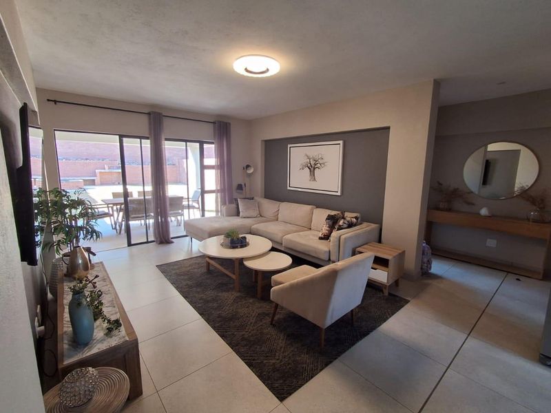 A well-maintained living room featuring large format floor tiles, a recessed feature wall, and sliding glass doors providing access to the outdoor patio area.