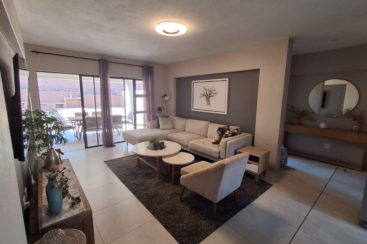 A well-maintained living room featuring large format floor tiles, a recessed feature wall, and sliding glass doors providing access to the outdoor patio area.