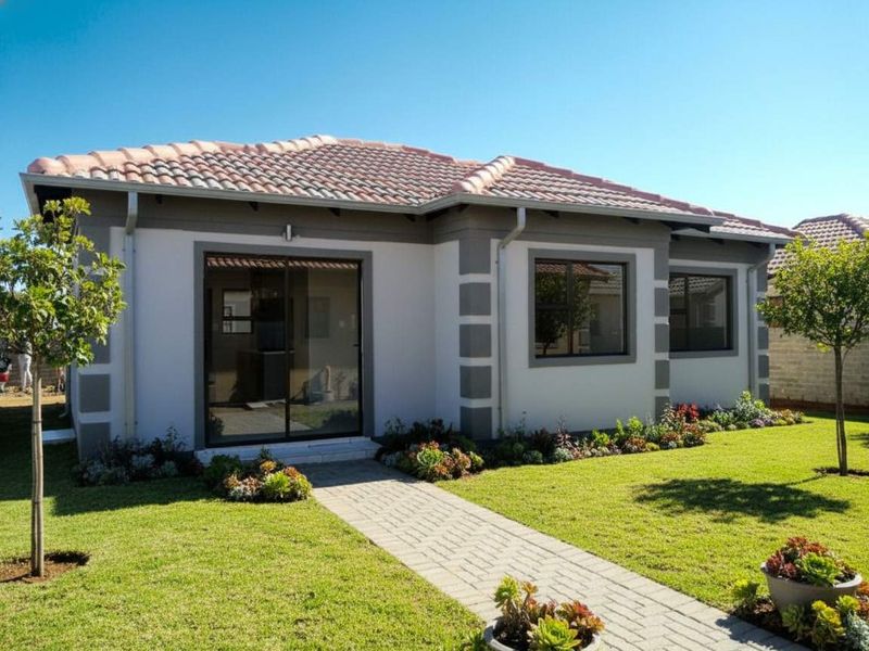 A well-maintained rear exterior view of a modern house featuring a tiled roof, paved walkway, and a neat landscaped garden.