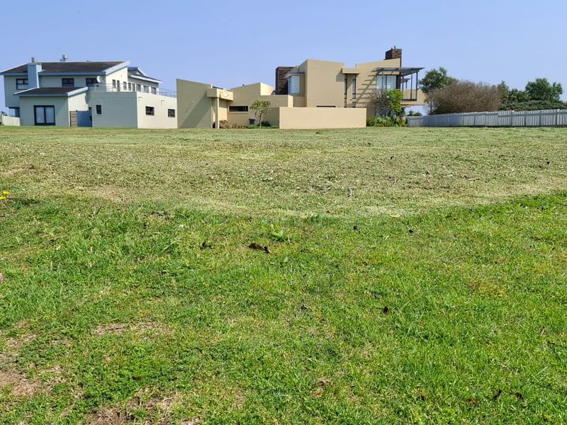 A clear, level residential vacant land plot featuring well-maintained grass, situated in a developed neighborhood with surrounding modern homes.