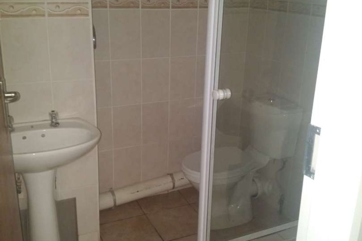 A compact bathroom featuring a pedestal basin, toilet, and a shower enclosure with tiled finishes. The space includes an exposed plumbing pipe.