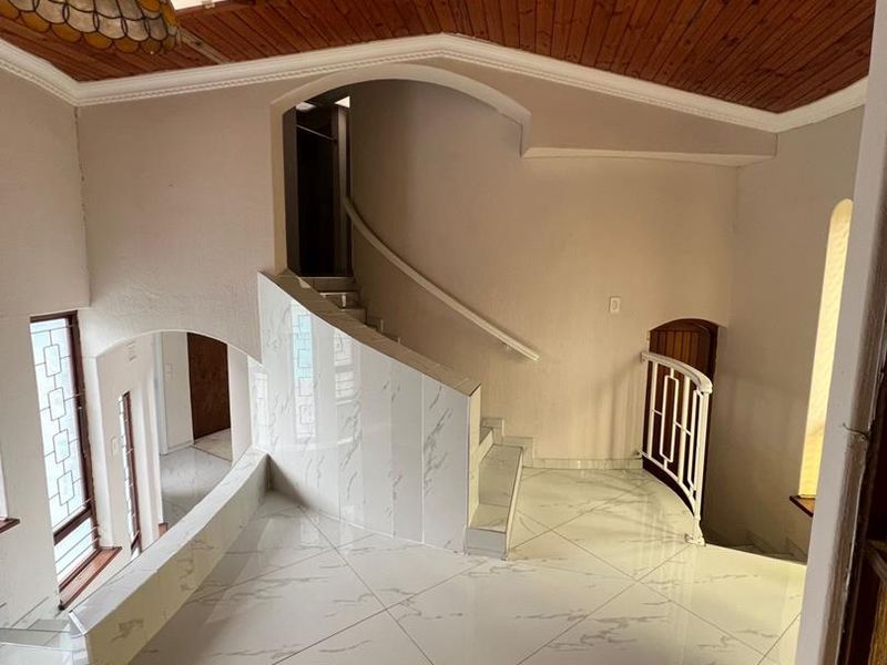 Spacious entrance hall featuring a high timber-clad ceiling, polished marble-look floor tiles, and an elegant staircase with a decorative wrought iron balustrade.