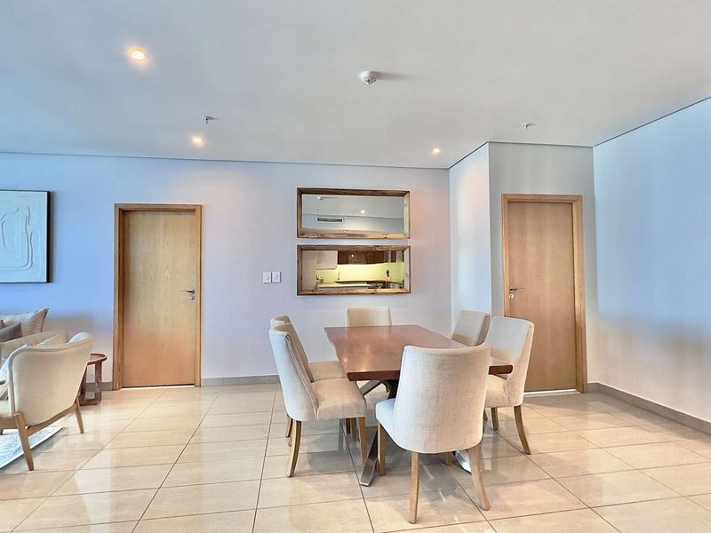 Spacious open-plan living and dining area featuring neutral tiled flooring, recessed lighting, and timber doors, with a convenient pass-through window to the kitchen.