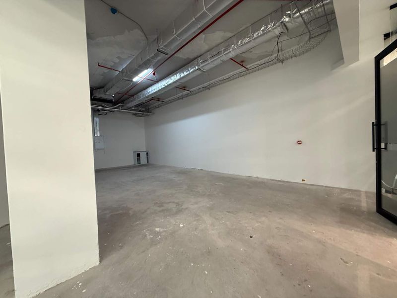 An empty, unfinished commercial retail space featuring exposed HVAC ducting, fire sprinkler systems, and raw concrete flooring, ready for custom fit-out.