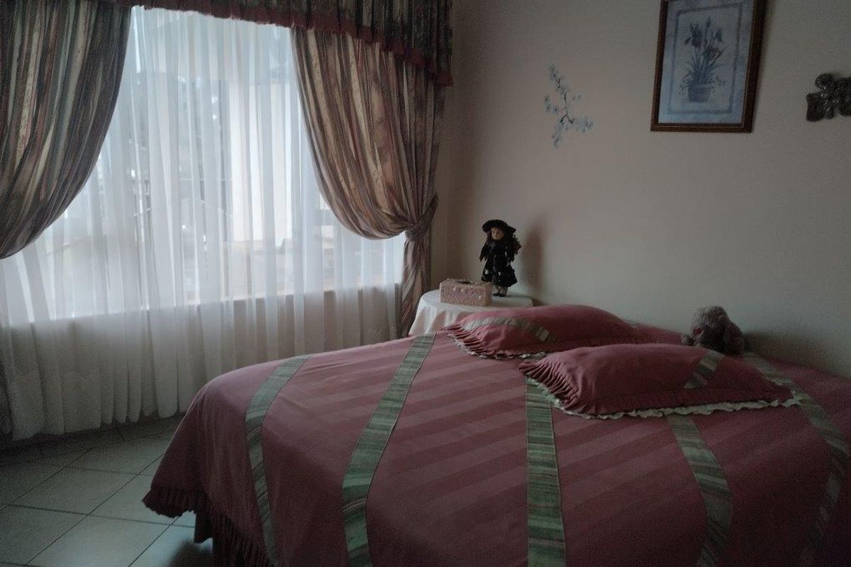 A bedroom featuring tiled flooring and a large window with curtains, providing natural light to the space.