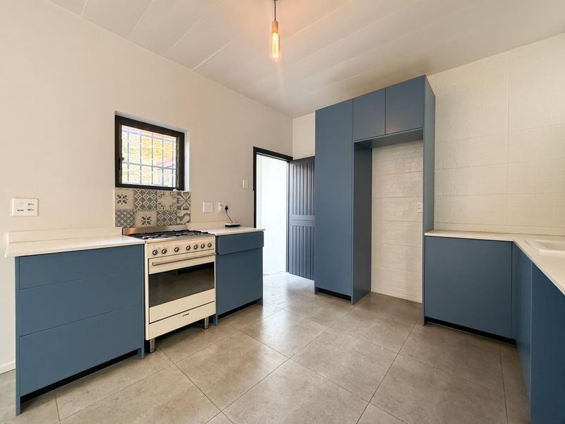 A modern, clean kitchen featuring blue cabinetry, a gas stove, tiled flooring, and a decorative tiled backsplash, offering a bright and functional workspace.