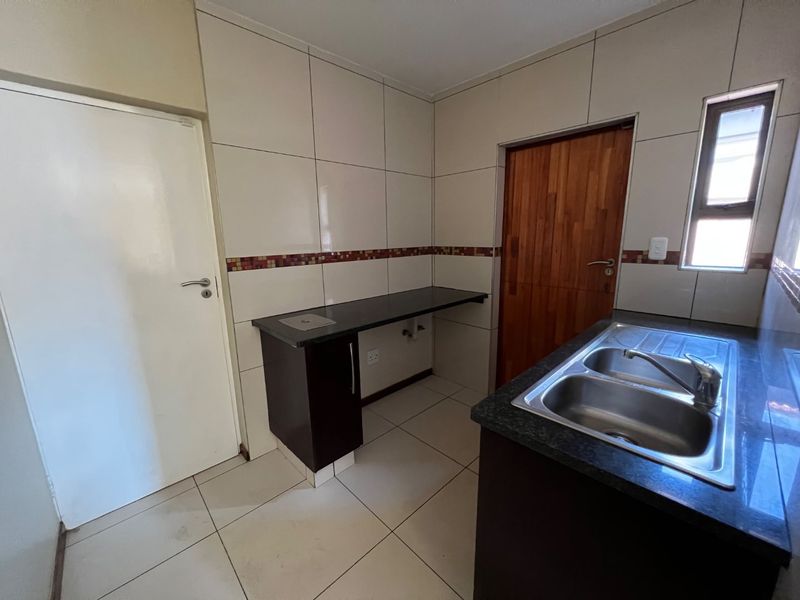 A clean and functional scullery featuring granite countertops, a double bowl stainless steel sink, tiled walls, and ample built-in cabinetry.