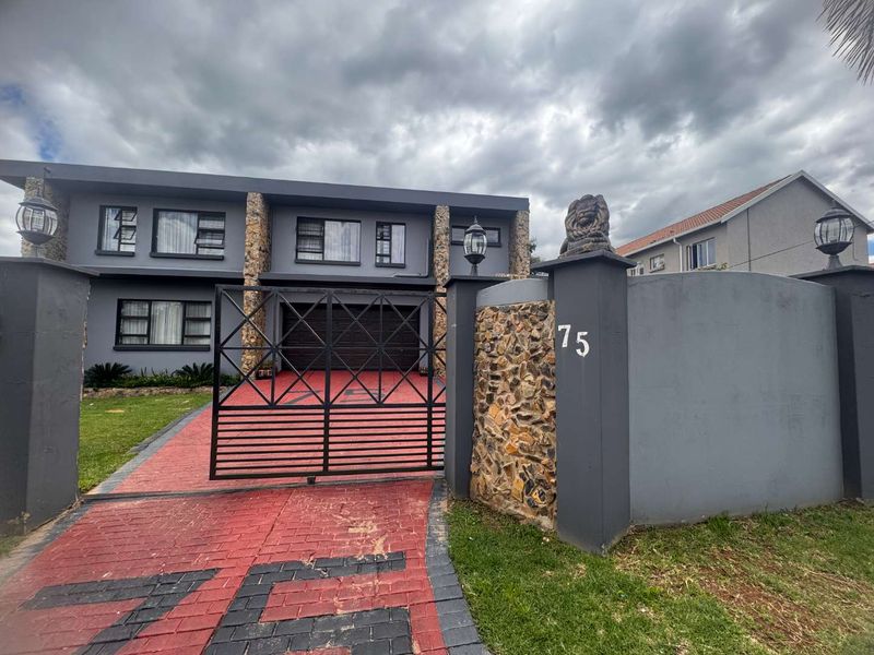 Front elevation of a two-story house featuring stone cladding accents, a paved driveway, and a secure gated entrance with a boundary wall.