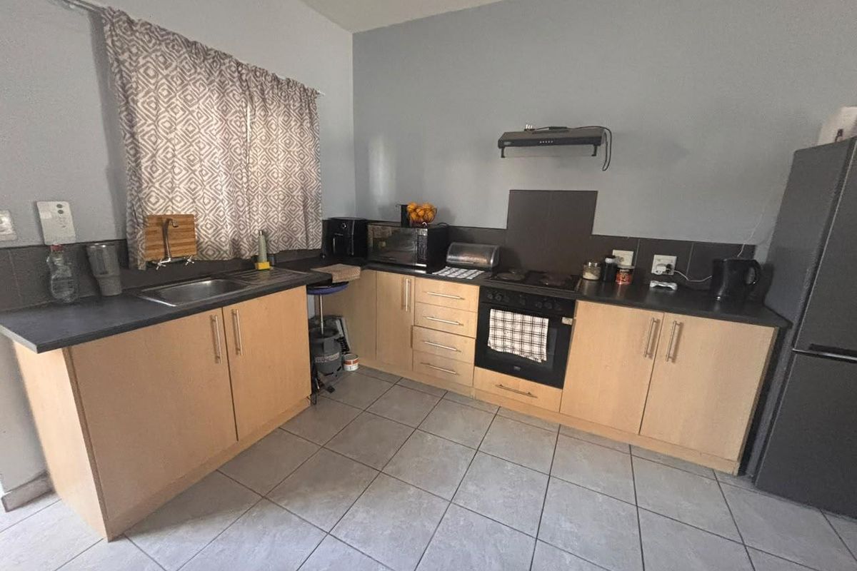A functional kitchen featuring light wood-finish cabinetry, dark countertops, tiled backsplash, and built-in cooking appliances including an oven and extractor fan.