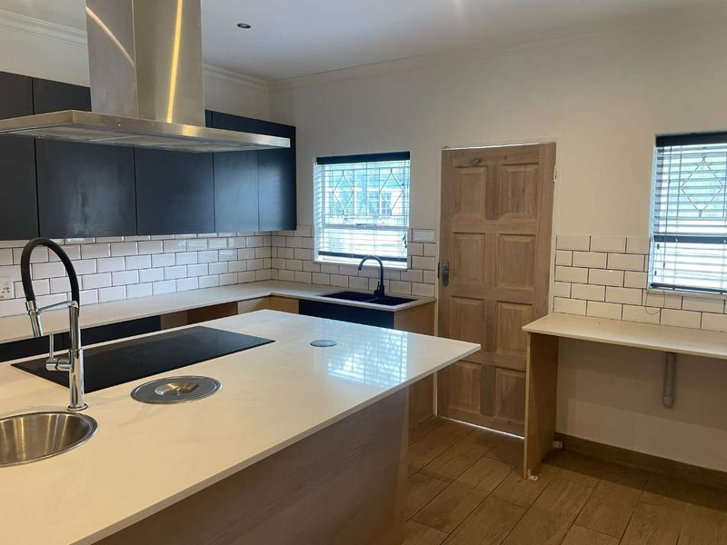 Modern kitchen featuring a central island with built-in hob, sleek cabinetry, subway tile backsplash, and wood-look tile flooring in a clean, contemporary space.
