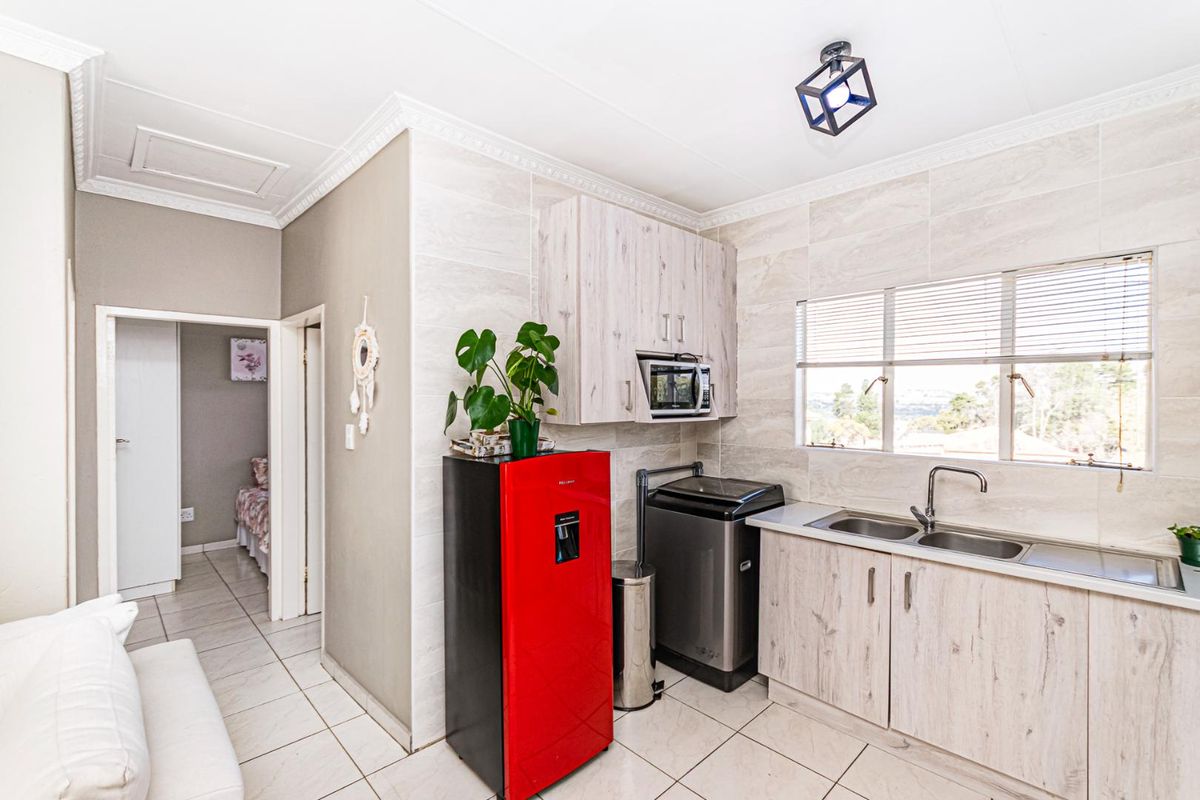 Compact kitchen area featuring light wood-grain cabinetry, tiled walls, double stainless steel sink, and integrated microwave space.