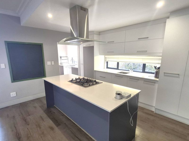 Modern kitchen featuring a central island with a gas hob, stainless steel extractor fan, ample white cabinetry, and sleek laminate flooring.