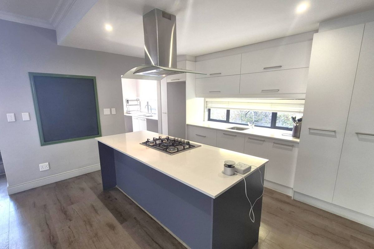 Modern kitchen featuring a central island with a gas hob, stainless steel extractor fan, ample white cabinetry, and sleek laminate flooring.