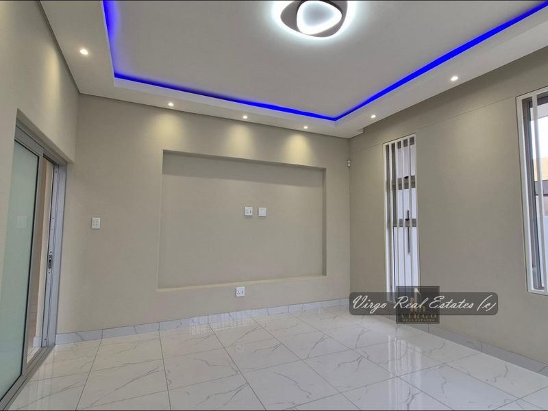 A modern, empty living room featuring polished porcelain floor tiles, a recessed television niche, and a contemporary ceiling design with integrated LED accent lighting.