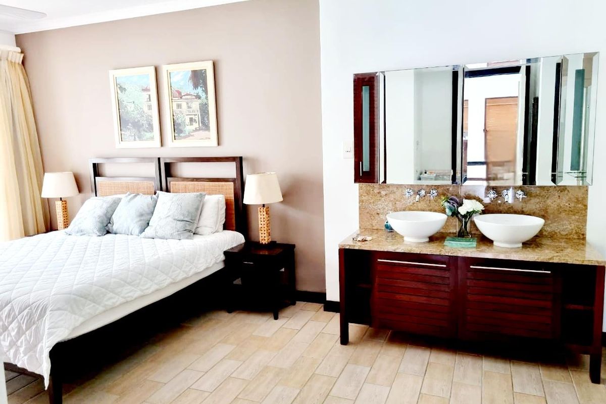 A bedroom featuring an open-plan vanity area with dual vessel sinks, granite countertop, and wooden cabinetry, integrated into the sleeping space.