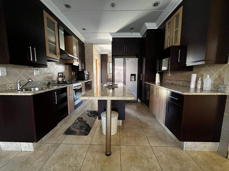 A spacious kitchen featuring dark cabinetry, granite countertops, a central island, and built-in appliances, offering a functional and well-lit culinary workspace.