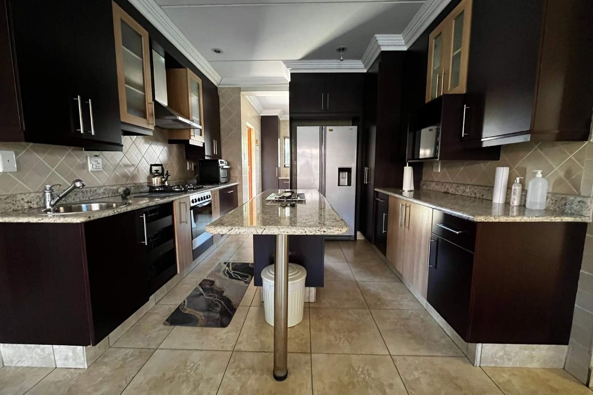 A spacious kitchen featuring dark cabinetry, granite countertops, a central island, and built-in appliances, offering a functional and well-lit culinary workspace.