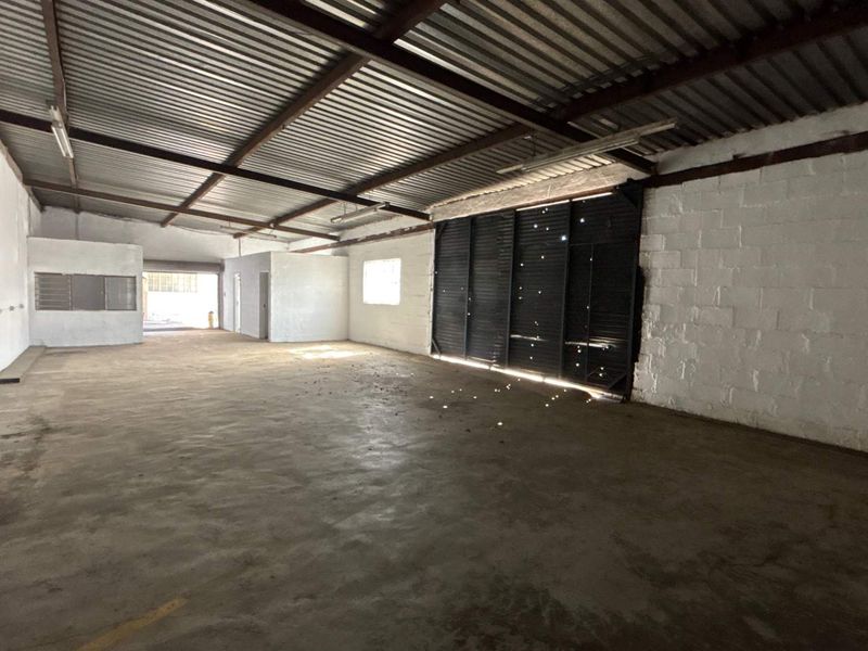 Spacious industrial utility area featuring exposed steel roof trusses, concrete flooring, and painted block walls, suitable for workshop or storage use.