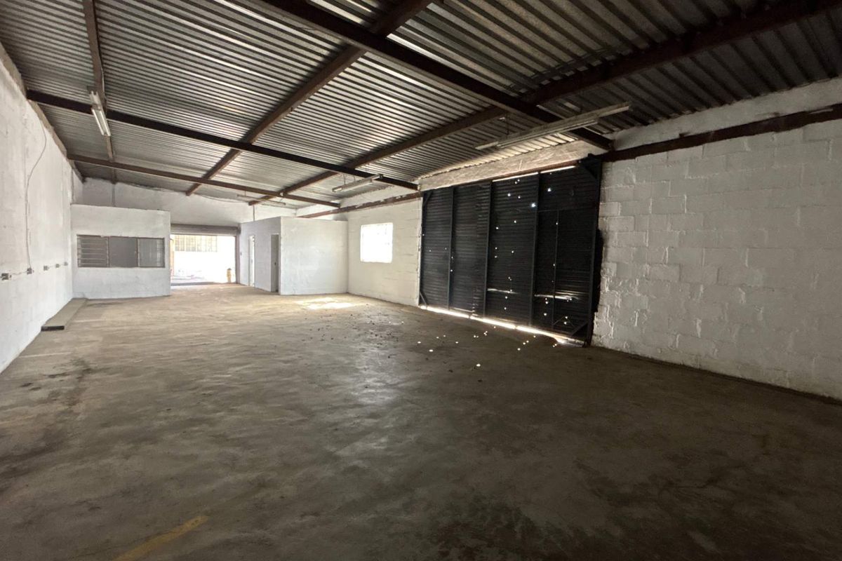 Spacious industrial utility area featuring exposed steel roof trusses, concrete flooring, and painted block walls, suitable for workshop or storage use.