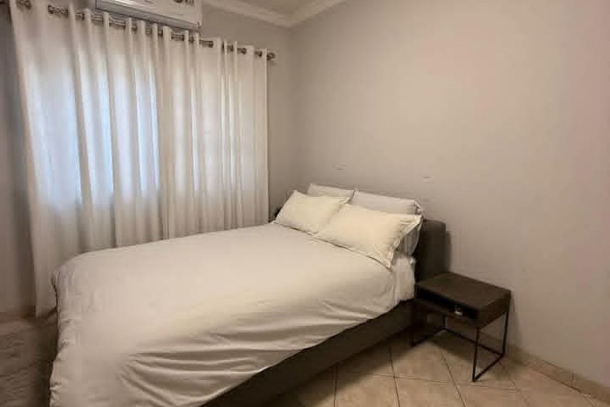 A functional bedroom featuring ceramic tile flooring, coving, and a wall-mounted split-system air conditioning unit.