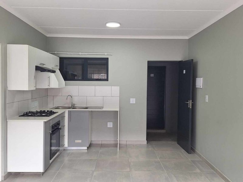 Modern open-plan kitchen featuring built-in cabinetry, gas hob, electric oven, and tiled flooring in a clean, neutral-toned living space.