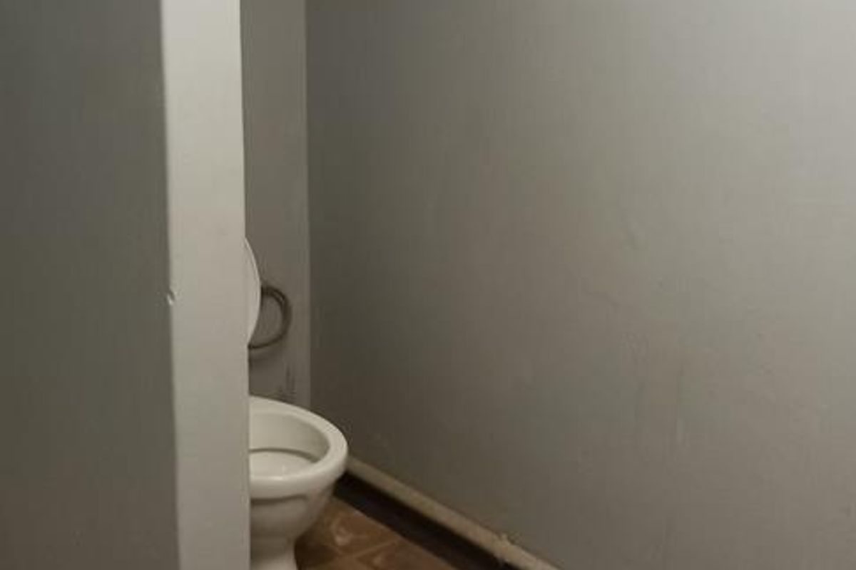 A small bathroom area featuring a toilet, partition wall, and multi-colored tiled flooring.