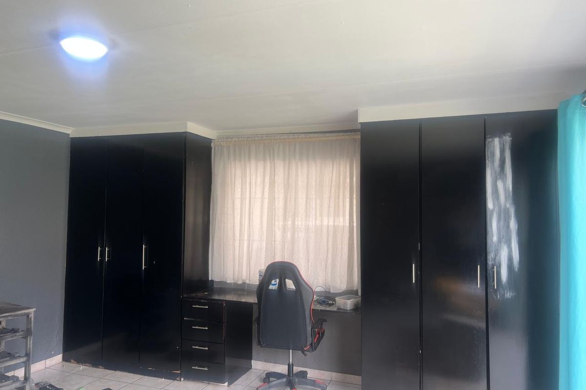 Bedroom featuring extensive built-in black cabinetry with an integrated desk area, tiled flooring, and a window with curtaining.