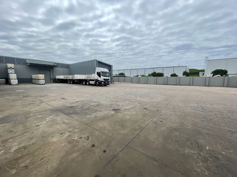 Spacious industrial concrete yard featuring perimeter walling and access to a warehouse facility with roller shutter doors.