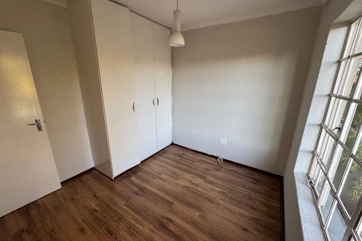 A bright bedroom featuring wood-look laminate flooring, built-in cupboards, and a large window allowing for natural light.