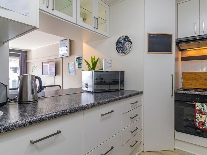 A well-maintained kitchen featuring white cabinetry, dark laminate countertops, a built-in electric oven with hob, and an extractor fan.