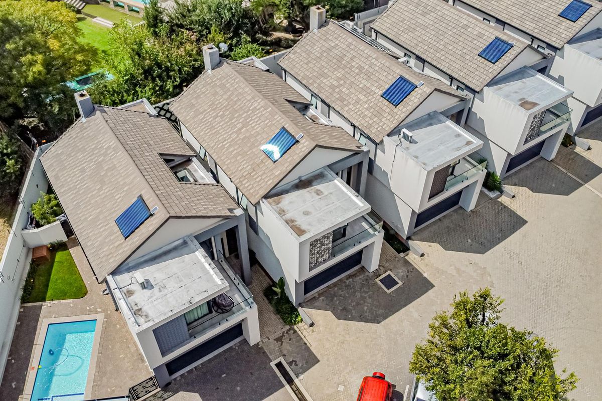 Aerial view of a modern cluster housing complex featuring tiled roofs, solar panels, private swimming pools, and paved driveway access.
