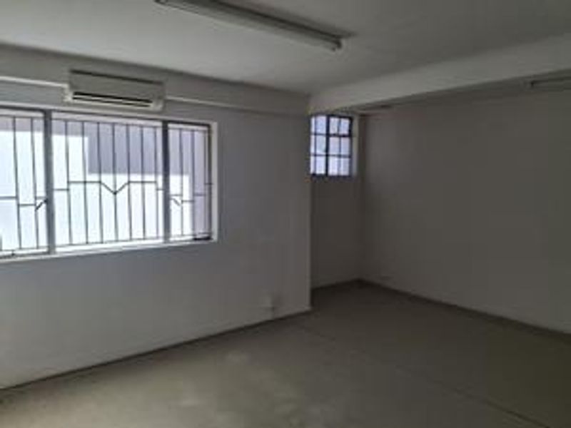 An empty office space featuring neutral walls, an integrated air conditioning unit, and security bars on the windows.