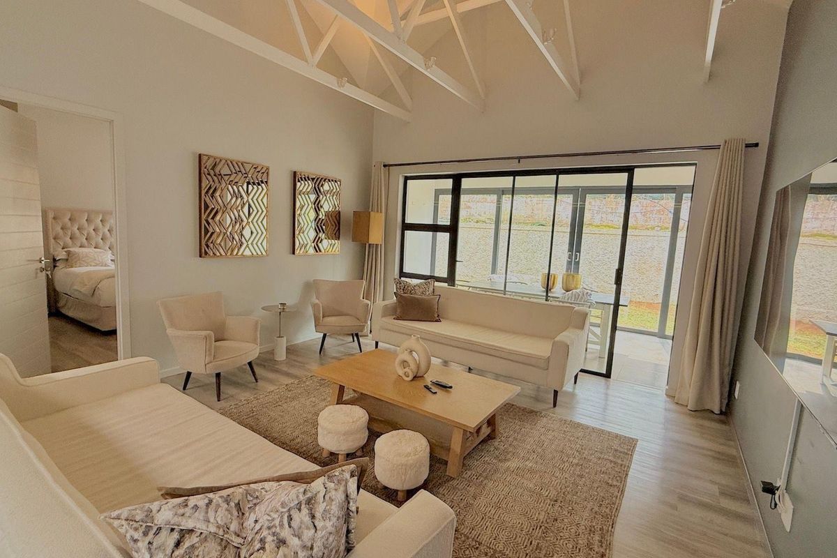 Spacious living room featuring high vaulted ceilings with exposed trusses, large sliding glass doors leading to the patio, and neutral wood-look flooring.