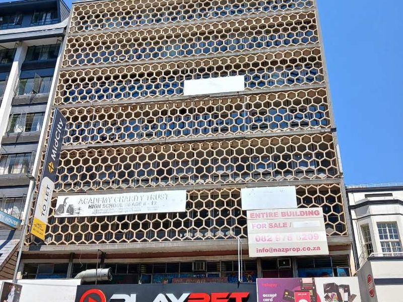 Front elevation of a multi-story commercial building featuring a distinctive honeycomb facade screen and ground-level retail storefronts.