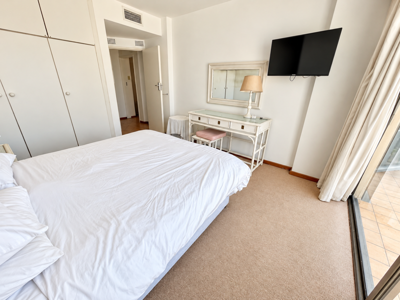 A bright bedroom featuring built-in cupboards, carpeted flooring, and a sliding glass door providing access to an outdoor balcony area.