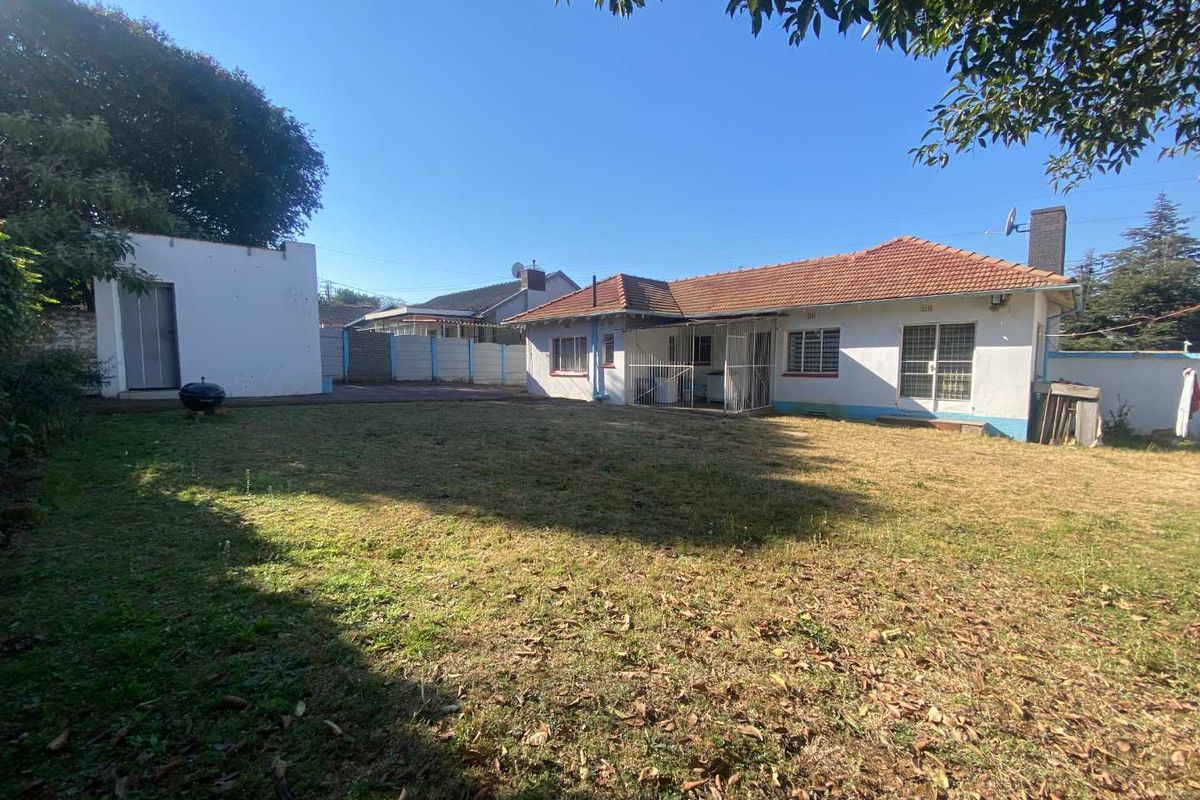 Rear view of the property featuring a tiled roof, security gates, and a detached outbuilding set within a spacious backyard.