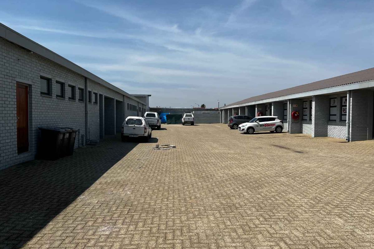 Exterior view of an industrial complex featuring a paved courtyard area with multiple unit access points and perimeter brick walling.